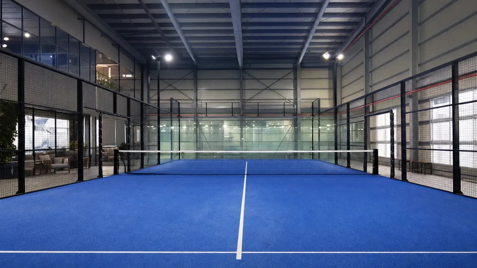 Empty indoor padel court with glass walls and blue turf