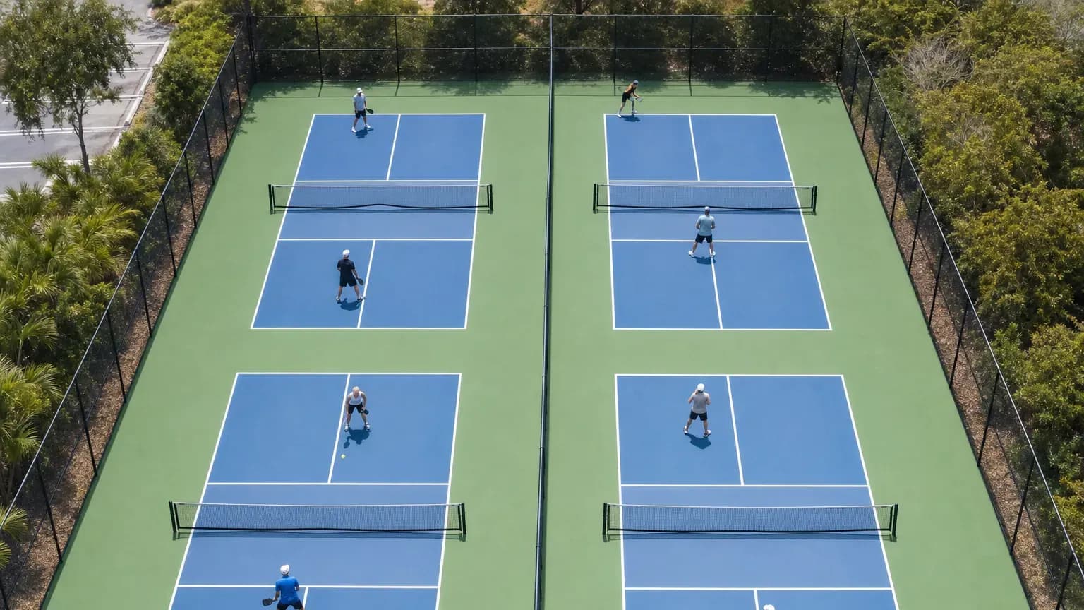 Overhead view of four pickleball courts with white lines and runoff space inside one fenced enclosure.